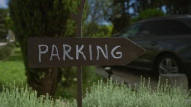 Kırsal park levhası arka planda park etmiş bir arabanın bulunduğu yeşil bir bahçede yolu gösteriyor..