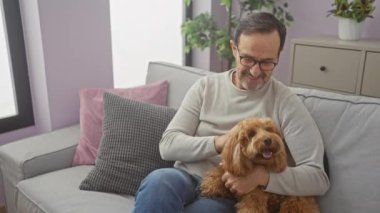 Orta yaşlı İspanyol bir adam sıcak bir oturma odasında neşeli bir kanişi okşuyor.