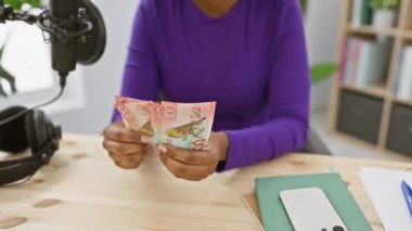 Mor gömlekli Afro-Amerikalı bir kadın radyo stüdyosunda yeni Zelanda dolarları sayıyor..