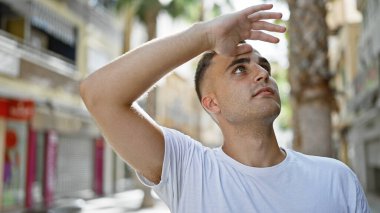 Yakışıklı bir genç adam, şehir sokağında dikilirken gözlerini güneşten koruyor..