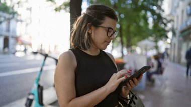 Neşeli İspanyol kadın neşe içinde Madrid 'in canlı caddelerinde akıllı telefon kullanıyor. Gözlükleri şehrin çekiciliğini yansıtıyor. Muhteşem gülümsemesi cep telefonunda sohbet ediyor..