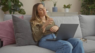 Genç, güzel bir kadın rahat bir kanepede dizüstü bilgisayarıyla rahat bir anın tadını çıkarıyor..