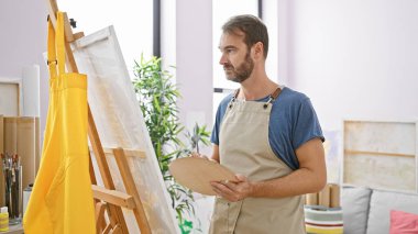 Düşünceli bir adam, tablosunu parlak bir sanat stüdyosunda incelerken palet tutar..