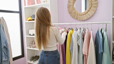 Sarışın bir kadın, günlük kıyafetlerini giyip, parlak bir evde giyiniyor ve moda tercihleri yapıyor..