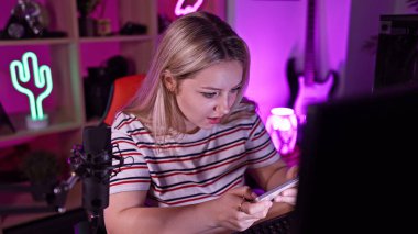 Sarışın kadın geceleri neon ışıklı oyun odasında akıllı telefon kullanırken odaklanmış..