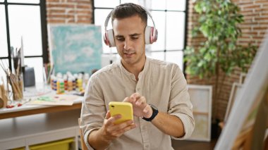 Bir sanat atölyesinde akıllı telefon kullanan kulaklıklı İspanyol bir adam..