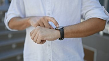 Gündelik tişörtlü genç bir İspanyol açık hava ortamında akıllı saatini kontrol ediyor..