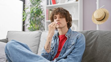 Düşünceli, kıvırcık saçlı ve kot ceketli genç bir adam. Kapalı bir koltukta oturuyor, dalgın dalgın dalgın bakıyor.