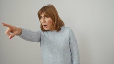 Kısa saçlı, şaşırmış orta yaşlı bir kadın beyaz arka planlı bir stüdyoda şok etkisi yaratıyor..