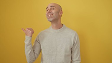 Sarışın, kel ve sakallı bir adam. Arka planda sarı bir duvar var. Pozitifliği ve yönü çağrıştırıyor..