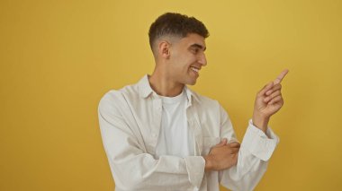 Yakışıklı bir genç adam gülümsüyor ve sarı bir arka plana işaret ediyor, pozitifliği ve güveni çağrıştırıyor..