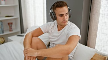 Düşünceli, genç, İspanyol bir adam, güzel ışıklandırılmış rahat bir odada kulaklık takmış, boş vakitleri ve iç gözlem anlayışını somutlaştıran bir yatakta oturuyor..