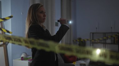 Genç bir kadın müfettiş, loş bir odada, polis bandının arkasında el feneri kullanarak olay yerini inceliyor..