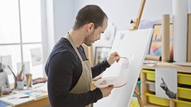 Parlak bir sanat stüdyosunun tuvaline sakallı kel bir adam resim yapıyor, yaratıcılık ve odaklanma tasvir ediyor..
