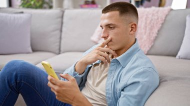 Modern oturma odasındaki koltukta akıllı telefon kullanan dalgın bir adam.