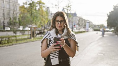 Güneşli Budapeşte caddesinde akıllı telefon kullanan esmer kadın.