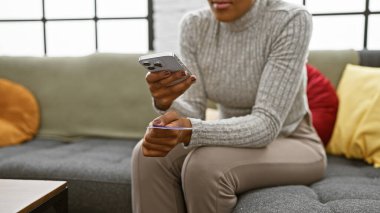 Genç Afro-Amerikalı kadın evde kredi kartının fotoğrafını çekmek için akıllı telefon kullanıyor.