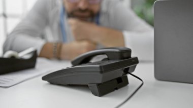 Ön planda bulanık bir telefonla evde oturmayı düşünen olgun sakallı bir adam profesyonel bir ortamda düşünceli davranır..