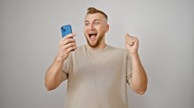 Sakallı heyecanlı genç adam, beyaz bir arkaplana karşı akıllı telefonu tutarak kutlama yapıyor..