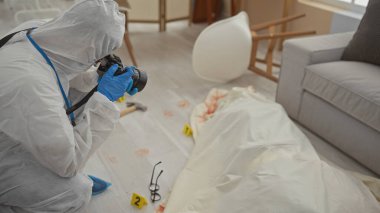 Koruyucu adli ekipmanlı bir adam olay yerinde kanıt fotoğrafı çekiyor, kanlı ayak izleri ve yerde bir ceset izi var..