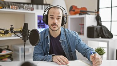 Müzik stüdyosunun içindeki mikrofonda enstrümanlı kel, kulaklıklı adam..