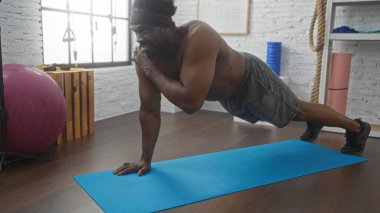 Yakışıklı Afrikalı Amerikalı bir adam spor salonundaki mavi bir paspasın üzerinde egzersiz yapıyor, güçlü ve iyi donanımlı bir spor merkezinde odaklanıyor..