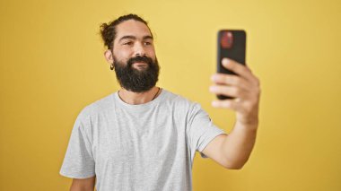Sakallı yakışıklı İspanyol bir adam sarı duvara karşı selfie çekiyor..