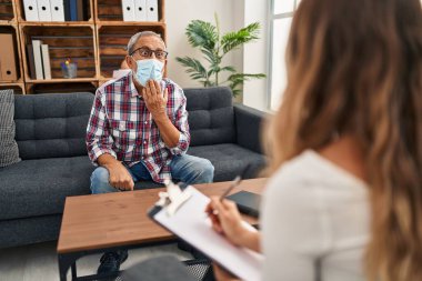 Şok olmuş tıbbi maskeli adam ağzını eliyle kapatıyor, şaşırmış sessizlik ifadesi. Psikoloji kliniğinden, konuşma korkusundan..