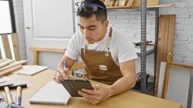 Yakışıklı, genç bir İspanyol, kapalı alanda iyi donanımlı bir marangoz atölyesinde plan yapmak için tablet kullanıyor..