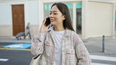 Telefondaki Asyalı kadın şehir caddesinde yürüyor, şehir yaşam tarzını ve bağlantılarını çağrıştırıyor.