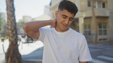 Yakışıklı genç adam, kentin arka planında acı ya da stresi tasvir eden bir rahatsızlıkla boyuna dokunuyor..