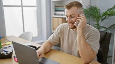 Modern ofis ortamında laptop ve cep telefonu kullanan yakışıklı sakallı adam.