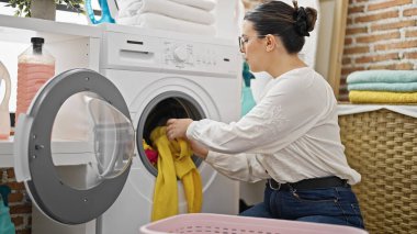 Genç ve güzel İspanyol kadın çamaşırhanedeki çamaşır makinesine çamaşır koyuyor.
