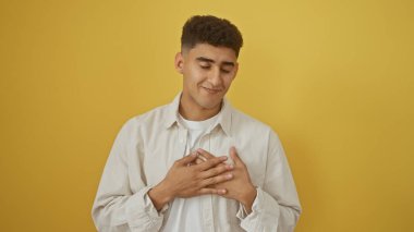 Minnettar genç adam gözleri kapalı, elleri yüreğinde, sarı bir arka planda..