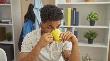 Yakışıklı Afrikalı Amerikalı adam, modern oturma odasında kahve içiyor..