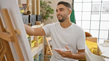 Parlak bir sanat stüdyosunda tuvale resim yapan yakışıklı sakallı adam..