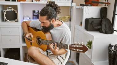 Ev stüdyosunda akustik gitar çalan sakallı yakışıklı bir İspanyol..