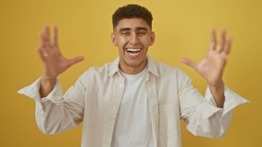 Sarı bir arka plana karşı kollarını kaldırıp gülen yakışıklı genç adam, neşe ve olumluluğu çağrıştırıyor..