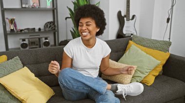 Neşeli bir Afrikalı Amerikalı kadın rahat bir oturma odasında kanepede uzanıyor..