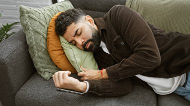 Genç bir İspanyol adam elinde akıllı bir telefonla kanepede kestiriyor, rahat bir apartman dairesinde..