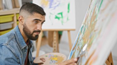 Sanat stüdyosunda tuvale resim çizen yakışıklı sakallı adam.