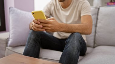 Evdeki bir kanepede oturan genç bir İspanyol, akıllı telefon kullanıyor ve ev ortamını resmediyor..