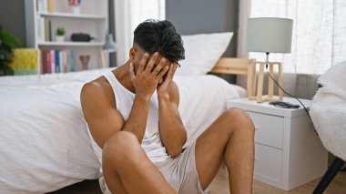 Işıl ışıl bir yatak odasındaki bir yatakta otururken sıkıntılı görünen genç bir İspanyol..