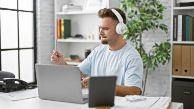 Kulaklıklı İspanyol bir adam modern ev ofis ortamında internetten çalışıyor..