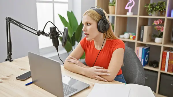 stock image Caucasian woman with blonde hair podcasting using a microphone and laptop in a studio setup.