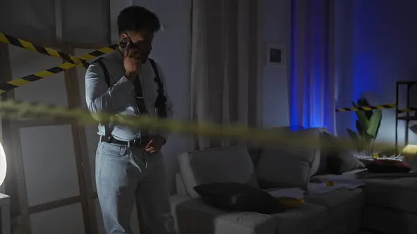 stock image African american man dressed as a detective in a dim crime scene room with caution tape talking on a phone.