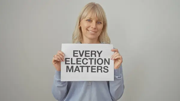 Stock image A confident middle-aged blonde woman holding a sign that reads 'every election matters' against a white backdrop