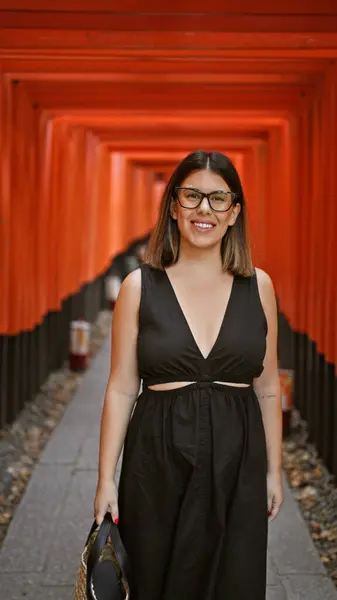 stock image Gorgeous hispanic woman in glasses flaunting a radiant smile at the majestic torii gates of fushimi inari-taisha, kyoto