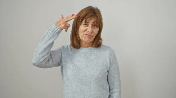 stock image Mature woman making a hand gun gesture to her head with a grimace, against an isolated white background.