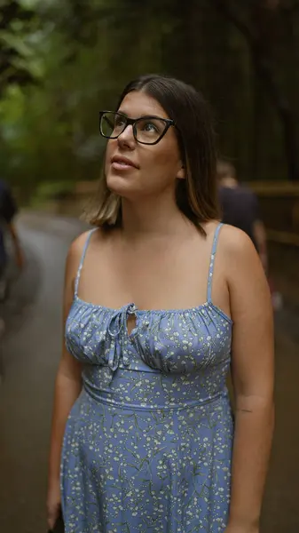 stock image Beautiful hispanic woman with glasses, smiling confidently as she stands amongst kyoto's lush bamboo forest, looking around, full of joy and amazement.